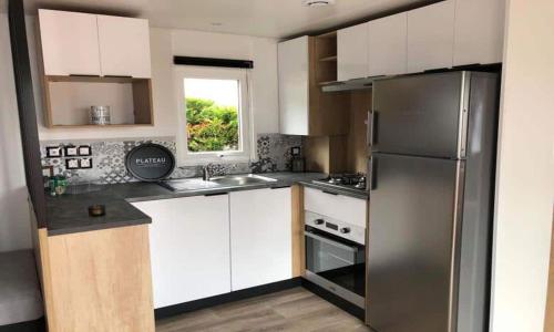 une cuisine avec des armoires blanches et un réfrigérateur en acier inoxydable dans l'établissement MH6pers-2ch-1sdb-lits faits-40m2-terrasse-tv--grand confort-empl calme-Kerlann, à Pont-Aven