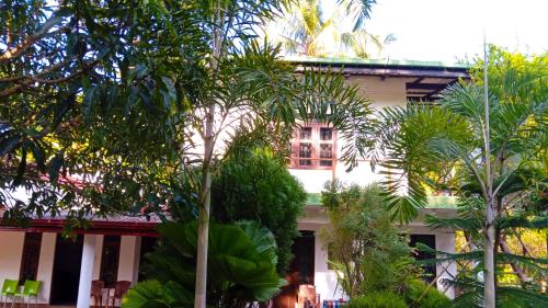 un bâtiment blanc avec des arbres devant dans l'établissement Sigiriya River Side Resort, à Sigirîya