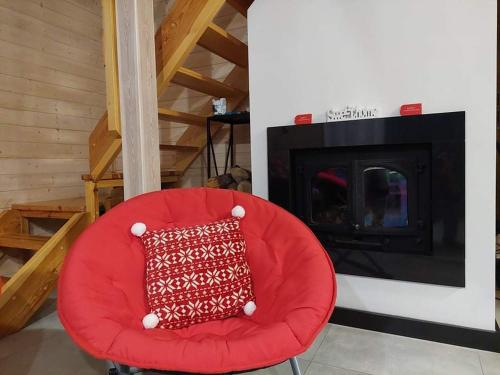 a red chair with a red pillow in front of a fireplace at Biały Żagiel - Dom do wynajęcia Pluski in Pluski