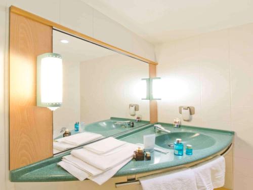 a bathroom with a sink, mirror, towel rack and towel dispenser at Hotel Ibis Firenze Nord Aeroporto in Sesto Fiorentino