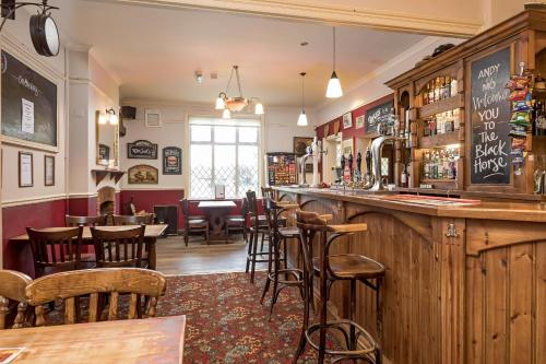 un bar dans un pub avec un bouquet de tabourets dans l'établissement The Black Horse, à Swaffham Bulbeck