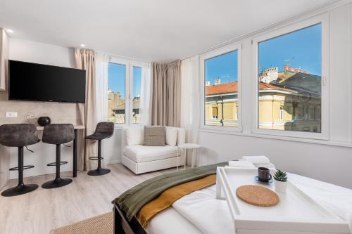 um quarto branco com uma cama, uma cadeira e janelas em Apartments Penkala em Rijeka