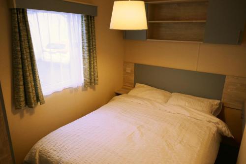 a bedroom with a white bed with a window at Plot 8 Lakeside Cabin, Wyldecrest, Millom in Millom