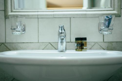 a white sink with two glasses and a mirror at Grand Hotel Dentro in Konitsa