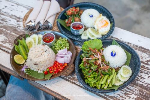 tres platos de comida en una mesa de madera en Silsopa Hostel en Nong Khai