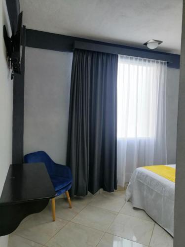 a bedroom with a bed and a blue chair and a window at Habitaciones del Pacifico in Zihuatanejo