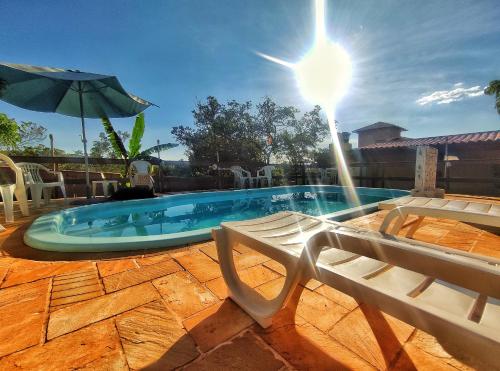 a swimming pool with two chairs and an umbrella at Topo do Cipó Ecopousada Vegana in Serra do Cipo