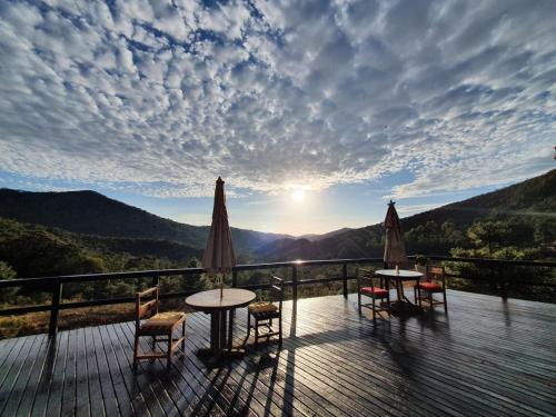 - deux tables et des chaises sur une terrasse en bois offrant une vue sur le coucher du soleil dans l'établissement Pousada do Morro Verde, à Carvalhos