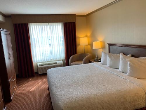 ein Hotelzimmer mit einem großen Bett und einem Stuhl in der Unterkunft Merit Hotel & Suites in Fort McMurray