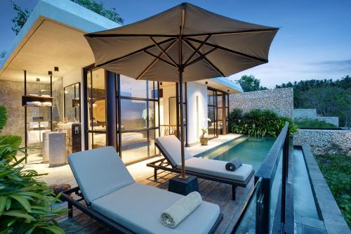 a patio with two chairs and an umbrella next to a pool at MAUA Nusa Penida Bali in Nusa Penida