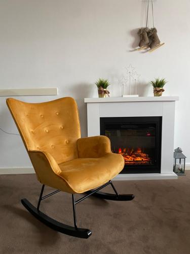 a yellow chair in a living room with a fireplace at Apartman Sky View, Župa Wellness & Spa u Centru Kopaonika in Kopaonik