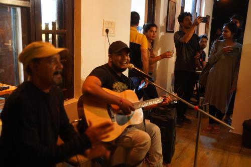 a group of people standing around a man playing guitar at Young Monk Hostel & Cafe Dharamkot in McLeod Ganj