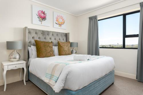 a white bedroom with a large bed and a window at Waters Edge Apartments in Cape Town