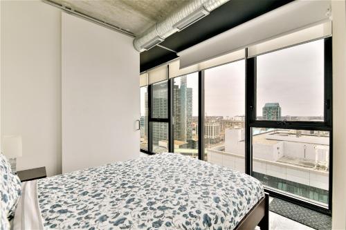 Cozy Skyline Condo in Downtown, across Canada Life Centre في وينيبيغ: غرفة نوم بسرير ونوافذ كبيرة