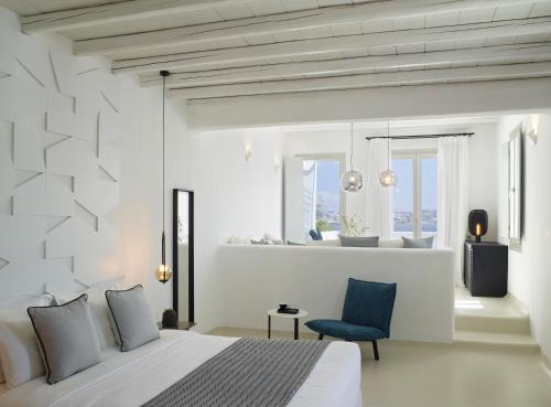 a white bedroom with a bed and a blue chair at Nimbus Mykonos in Agios Stefanos