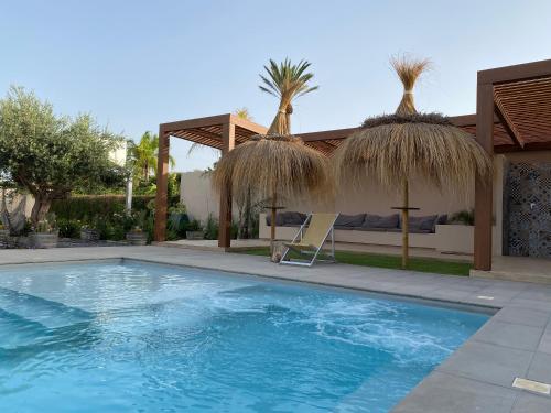 a swimming pool with two straw umbrellas and a house at Signorino Suites&Pool in Marsala