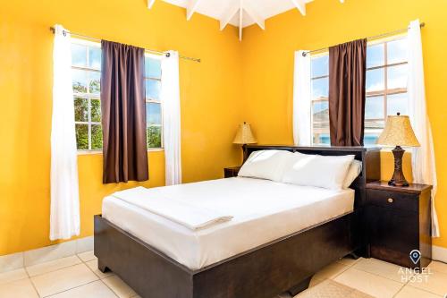 a bedroom with a bed with yellow walls and windows at Chalk Sound Beach Residences Near Sapodilla Bay Beach by Angel Host in Providenciales