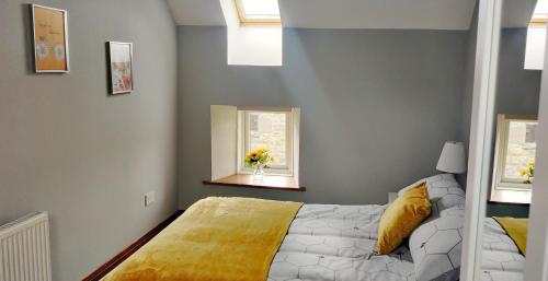 um quarto com uma cama com um cobertor amarelo e duas janelas em The Granary at Tinto Retreats, Biggar is a gorgeous 3 bedroom Stone cottage em Wiston