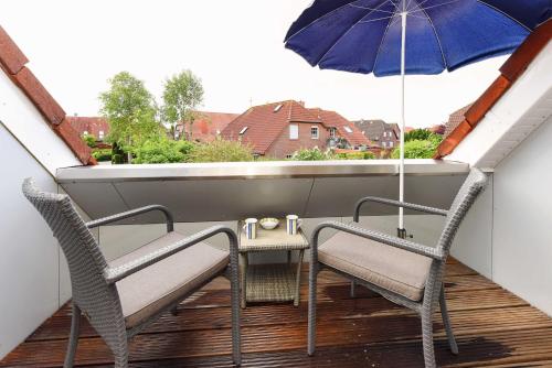 a balcony with two chairs and a table with an umbrella at Ferienwohnung Watt und Weite in Carolinensiel