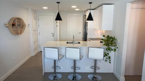 una cocina con armarios blancos y una isla de cocina con taburetes en Apartamento 1º Línea de Playa - Duna Beach, en Torrox Costa