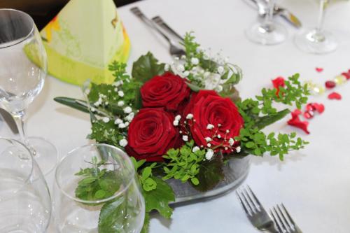 a vase of red roses on a table with wine glasses at Hotel Urirotstock in Isenthal