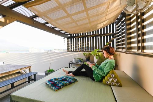 a woman sitting on a bench on a balcony at Green Guesthouse in Kagoshima