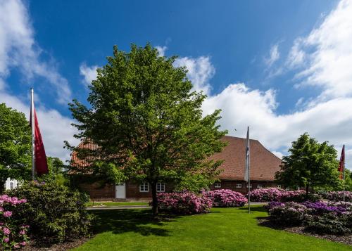 a building with a tree and flowers in a yard at Hotel Gut Kaden in Alveslohe