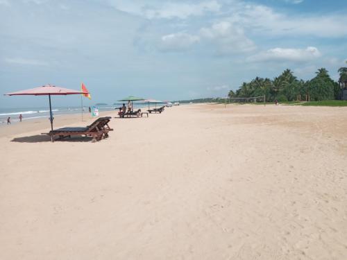 a sandy beach with picnic tables and an umbrella at Tharul Home in Bentota