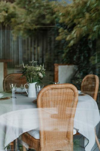 a table with wicker chairs and a white vase with flowers at Gîtes du Bulz, en pleine forêt proche de la mer in Pleyber-Christ