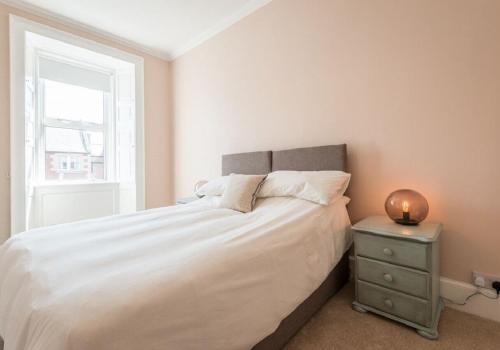 a bedroom with a white bed with a nightstand and a window at Greco's Close in Dunbar