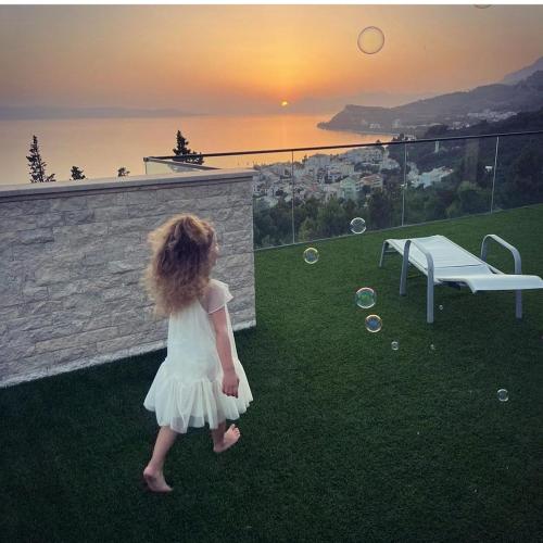 a little girl in a white dress standing on the grass at Villa Olive Hill in Tučepi