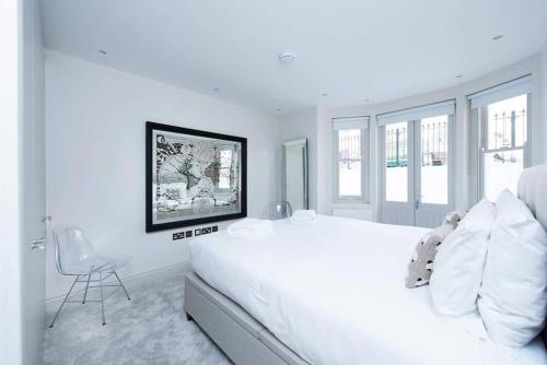 ein weißes Schlafzimmer mit einem großen Bett und einem Stuhl in der Unterkunft Beautiful 2BR flat with free parking in West London in London