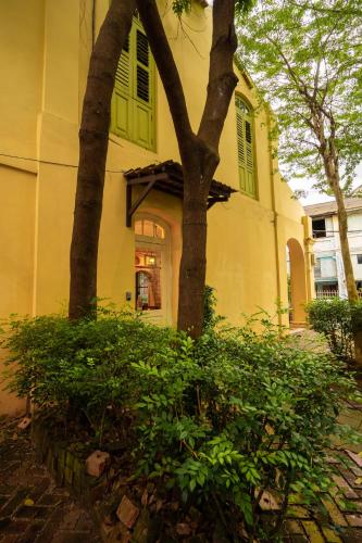 a yellow house with two trees and green bushes at Spices Hotel in George Town