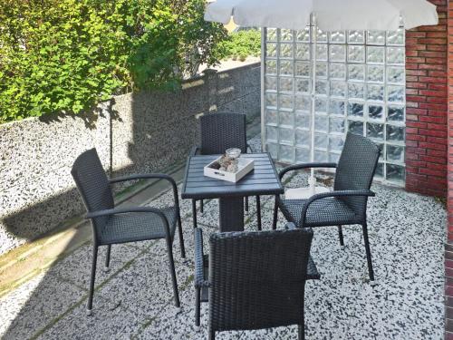 a table with three chairs and an umbrella on a patio at Apartment Am Koper Sand-1 by Interhome in Norddeich