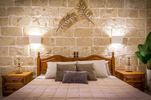 a bedroom with a bed with two lamps and a stone wall at Sweet Life Gozo - Boutique Living in Santa Luċija