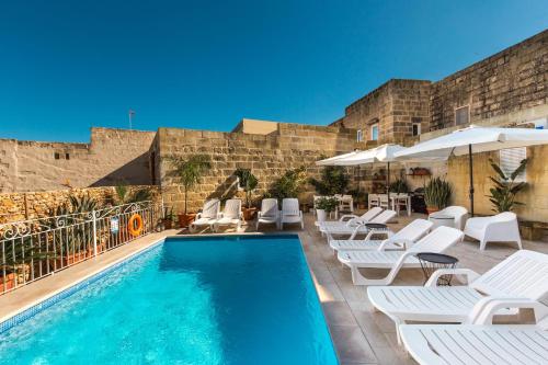 a swimming pool with white chairs and umbrellas at Sweet Life Gozo in Santa Luċija