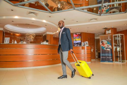 un hombre está tirando de una maleta amarilla en una tienda en Hotel Tiama Abidjan, en Abiyán
