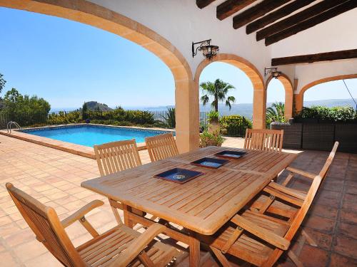 a wooden table and chairs on a patio with a pool at Holiday Home Nostra by Interhome in Jávea