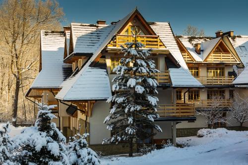 a log home with a snow covered tree in front of it at Aparthotel Bellamonte in Zakopane