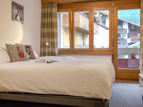 a bedroom with a large white bed and a window at Apartment Bellevue-6 by Interhome in Zermatt