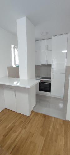 a white kitchen with white cabinets and a wooden floor at Stan na dan Bijeljina Niki in Bijeljina