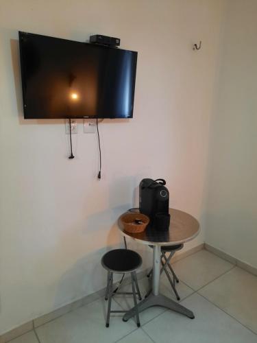 uma televisão pendurada numa parede com uma mesa e um banco em Xêpa Suítes Economy em São Miguel do Gostoso