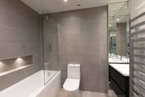 a bathroom with a toilet and a tub and a sink at Hampden Apartments - The Anne in Windsor