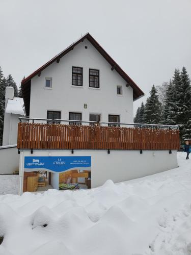 a white house with a deck on top of snow at HORSKÝ PENZION U SPLAVU in Josefuv dul