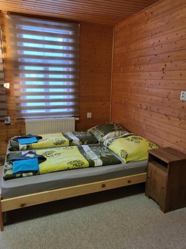 a bed in a room with a wooden wall at HORSKÝ PENZION U SPLAVU in Josefuv dul