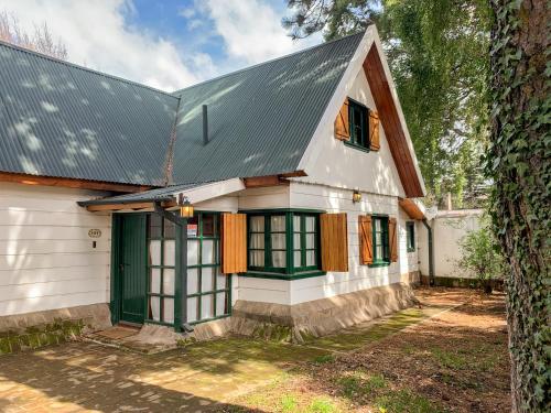 Casa blanca con ventanas verdes y techo metálico en El Barquito, en San Martín de los Andes
