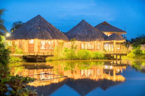 a group of huts with a reflection in the water at MEKONG SILT ECOLODGE in Can Tho