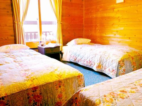two beds in a room with wooden walls and a window at Pension Buddy in Kitashiobara