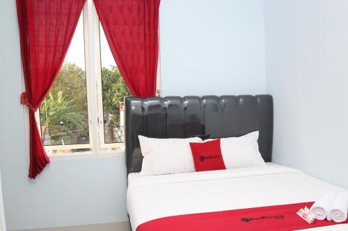 a bedroom with a bed with red curtains and a window at RedDoorz Syariah near Suncity Mall Madiun in Madiun