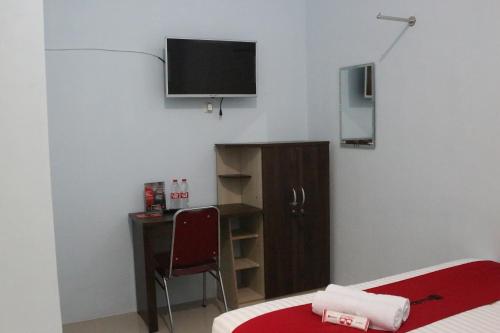 a room with a bed and a desk and a television at RedDoorz Syariah near Suncity Mall Madiun in Madiun